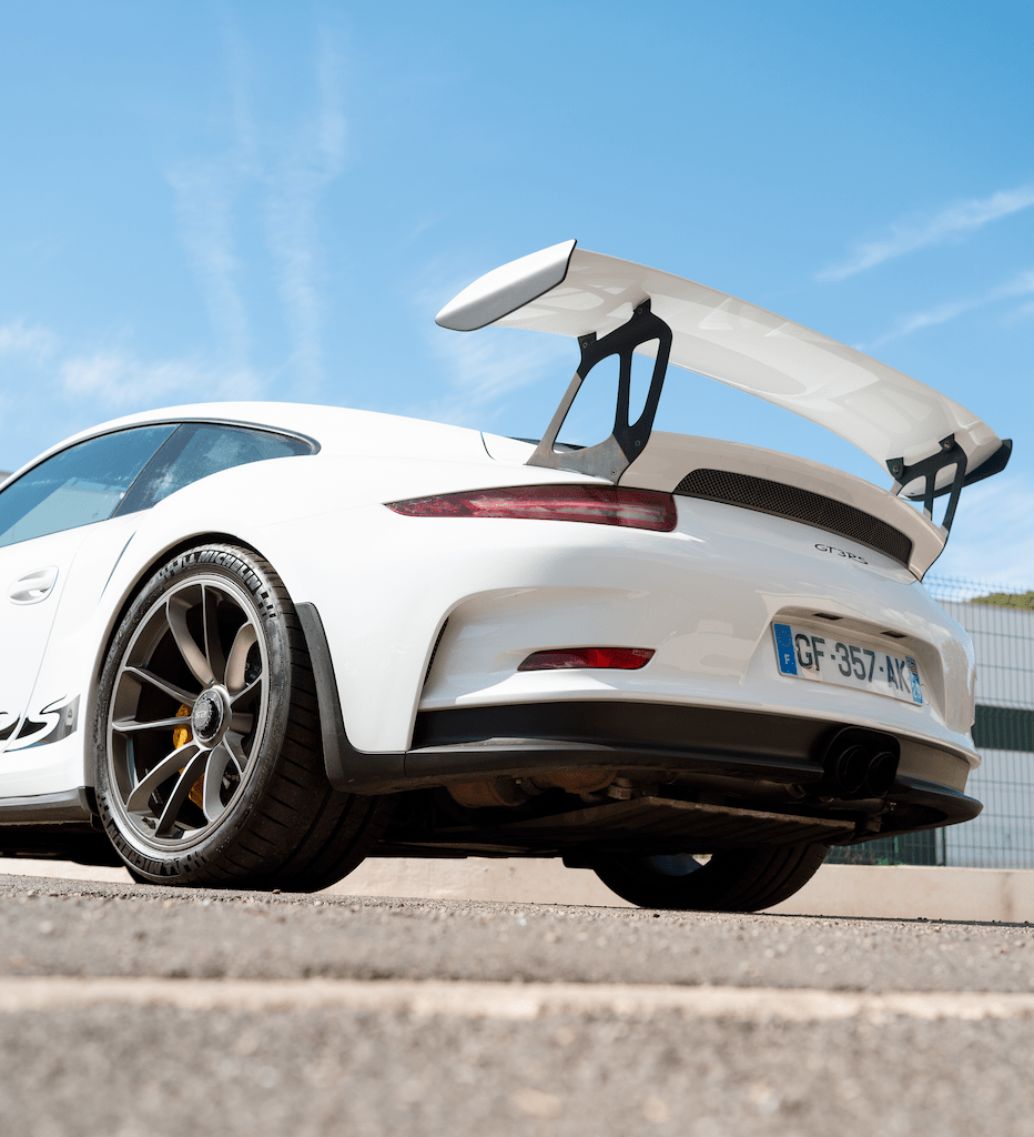 Photo de l'arrière d'une Porsche blanche avec le ciel bleu en arrière-plan.